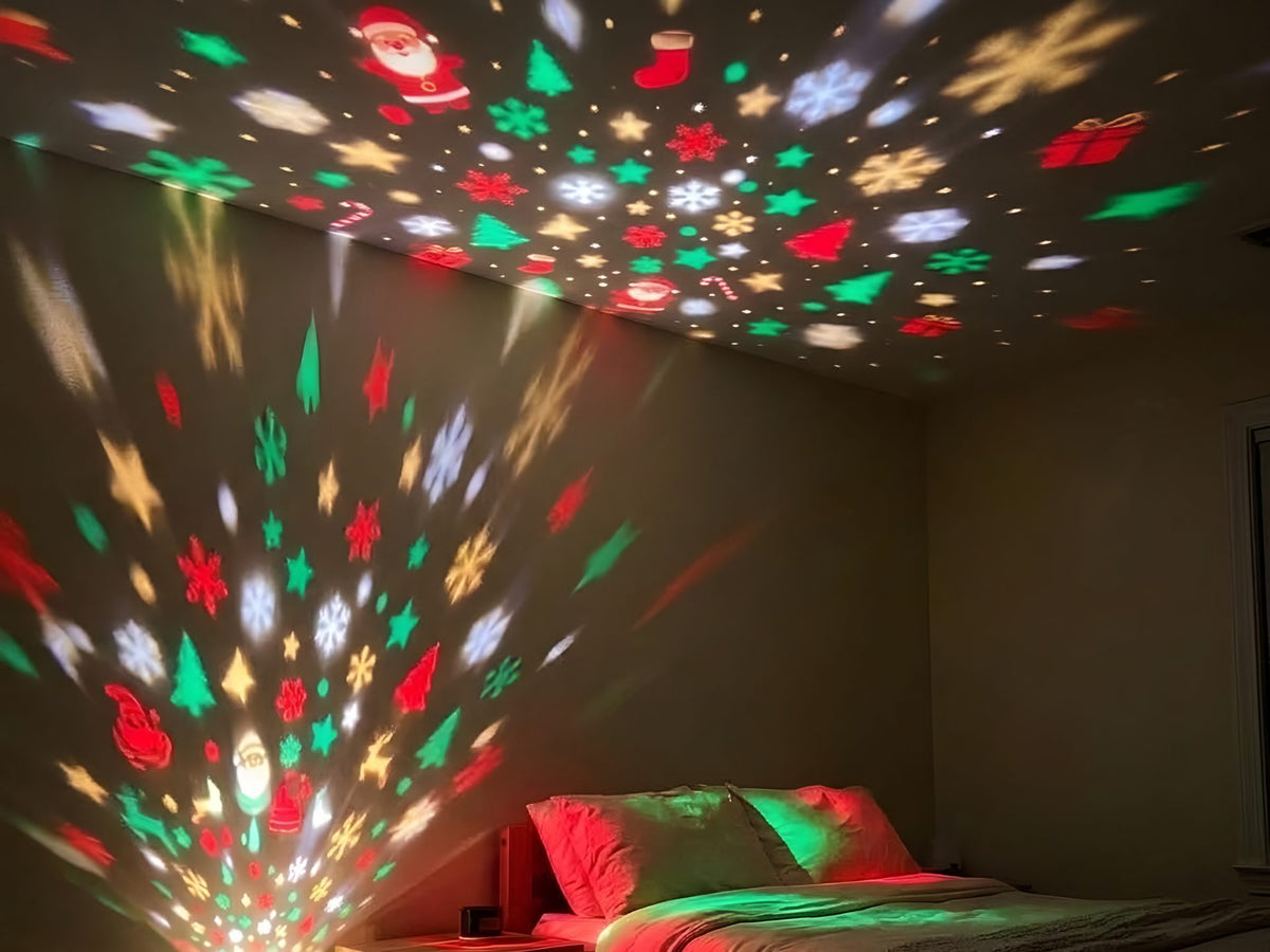 A dark bedroom with Christmas shapes across the ceiling and wall, the little tree glowing at the outlet