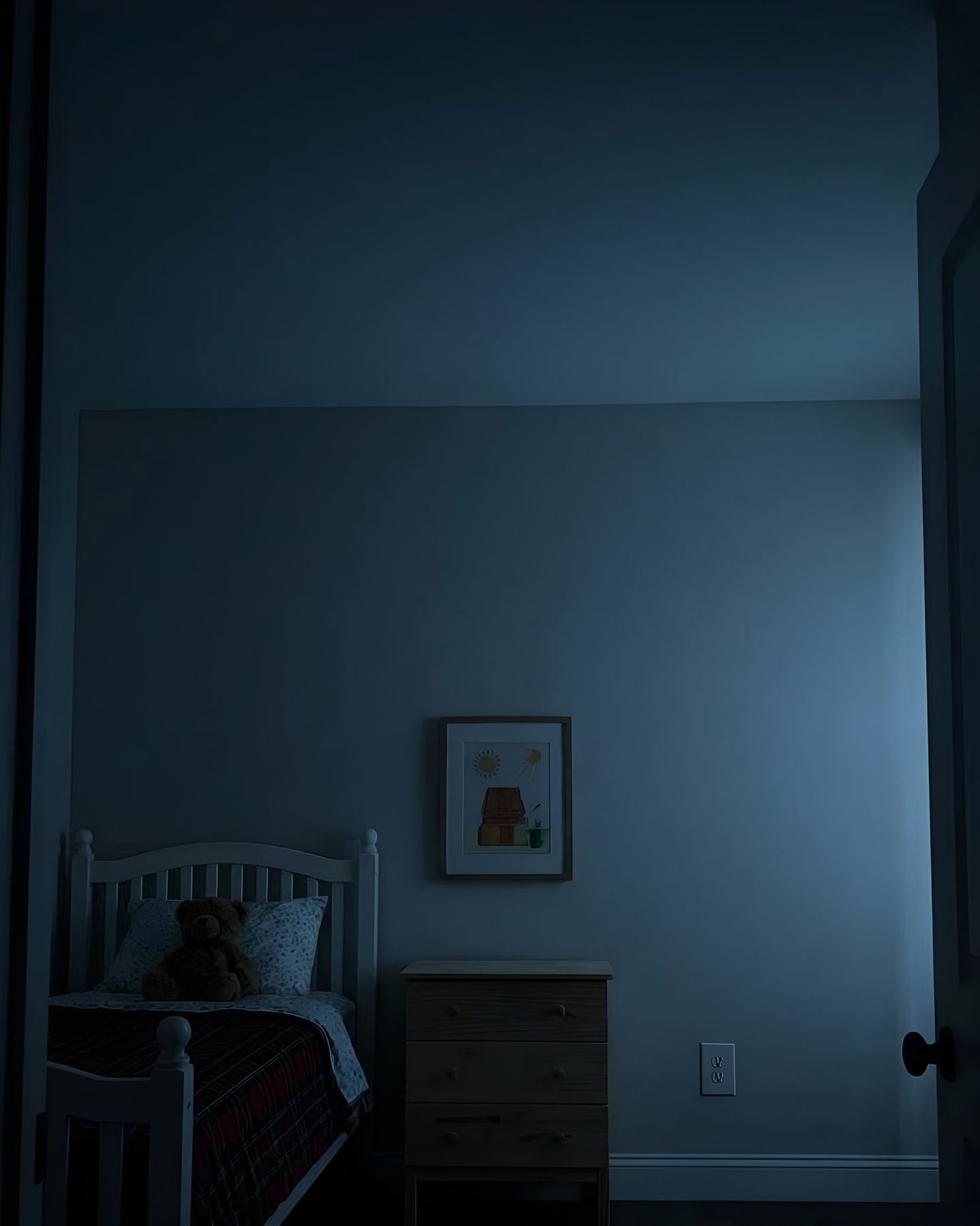 A kid's bedroom at night with every light off, the walls and ceiling plain and dark
