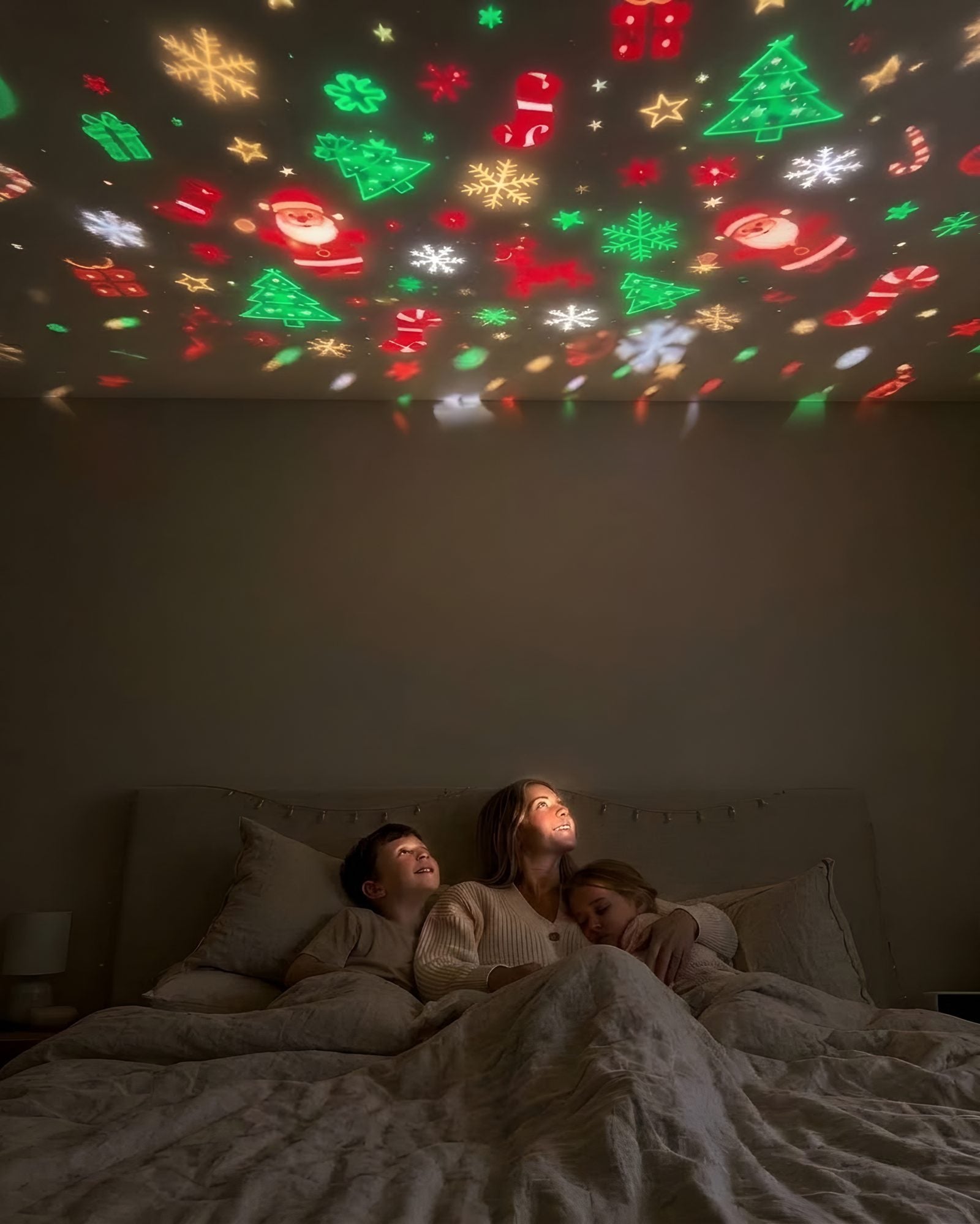 A mum and her two kids in bed, Santas and snowflakes covering the wall and ceiling