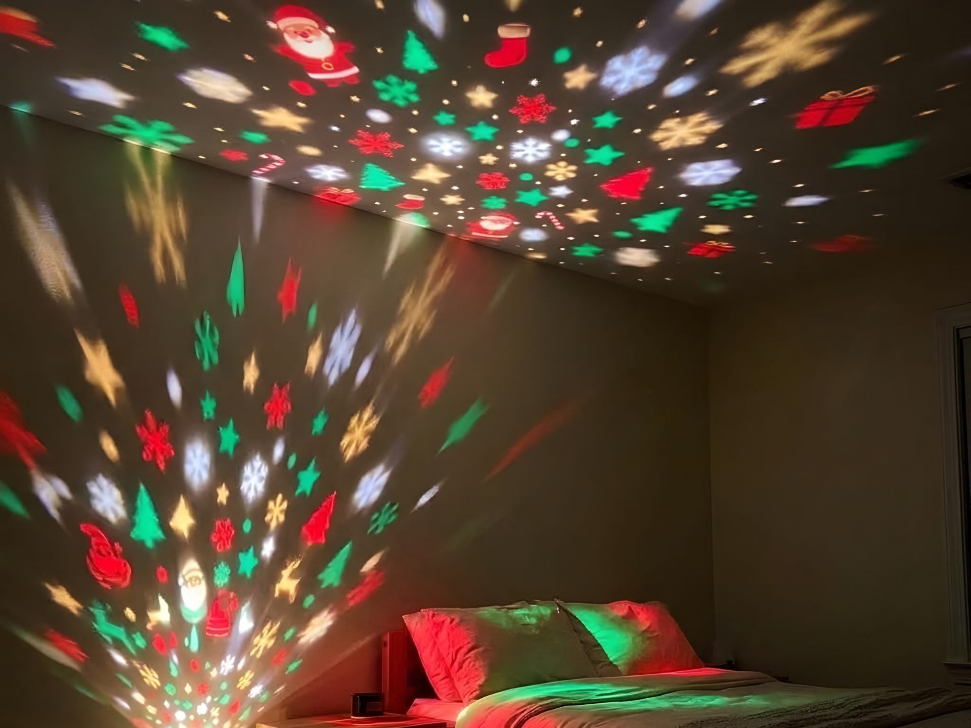 A dark bedroom with Christmas shapes across the ceiling and wall, the little tree glowing at the outlet